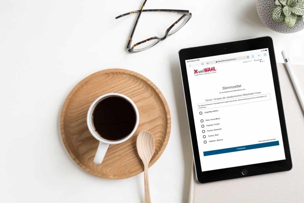 Tablet mit dem digitalen Stimmzettel von uniWAHL neben einer Tasse Kaffee
